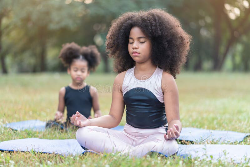 African American little girl sitting on the roll mat practicing meditate yoga in the park outdoor.