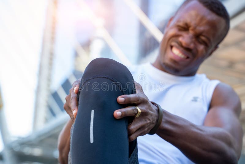 African American male runner bends over clutching his knee while in intense pain from an acute knee injury. stock photo African American male runner bends over clutching his knee while in intense pain from an acute knee injury. stock photo