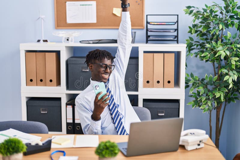 Lucrător din America Africană care utilizează smartphone cu expresie de câștigător la birou