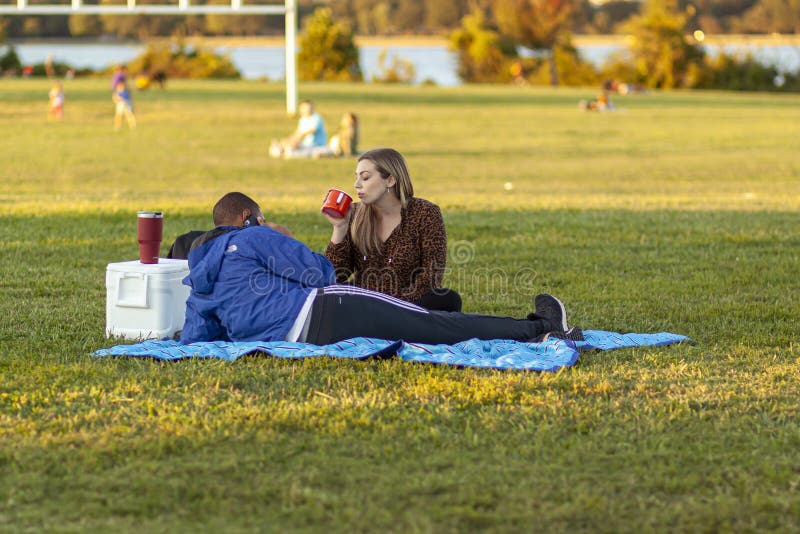 An African American man and a caucasian woman are relaxing in Gravelly Point park at a sunny afternoon.