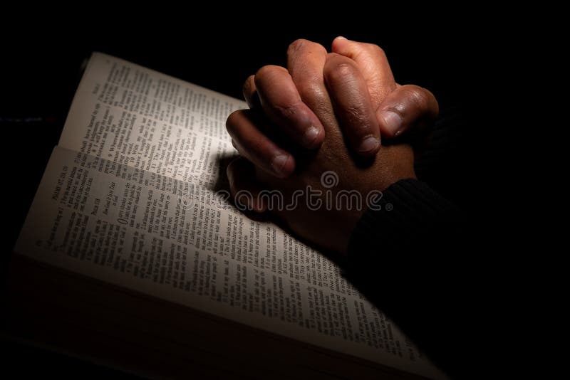 African American Man Praying with Hands on Top of the Bible on Dark Scene