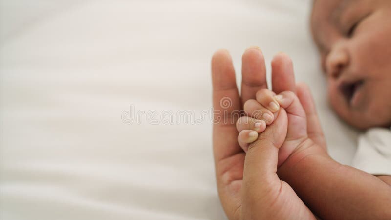 African american new born baby hand holding mom finger on white bed