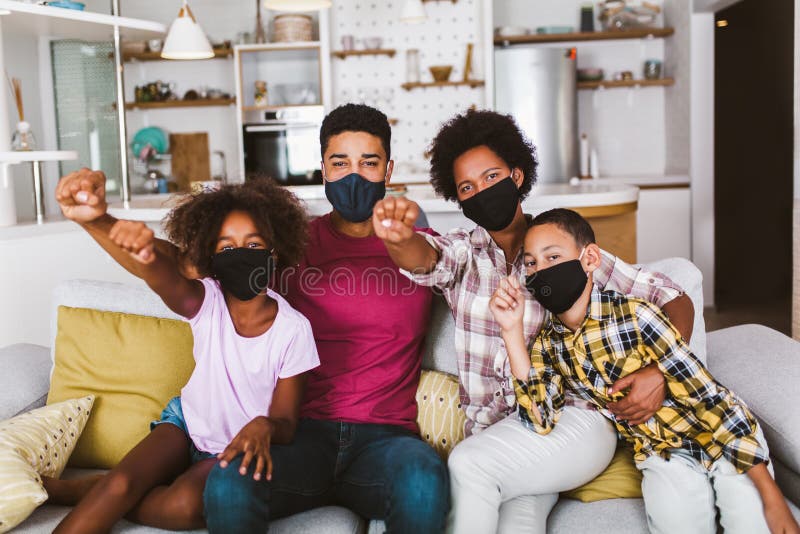 African American parents and cute small kids wearing protective masks at home. Stop the virus and epidemic diseases