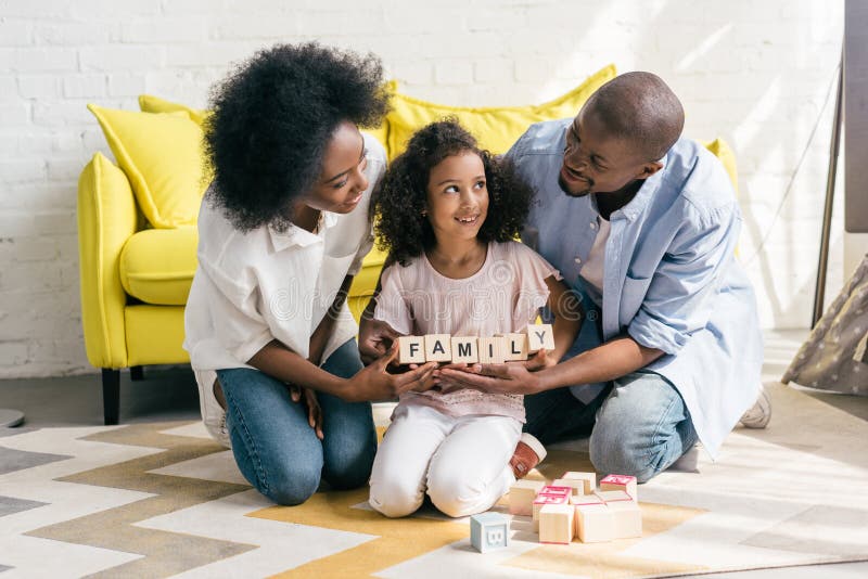 african american parents and daughter holding wooden blocks with family lettering together on floor royalty free stock photography african american parents and daughter holding wooden blocks with family lettering together on floor royalty free stock photography