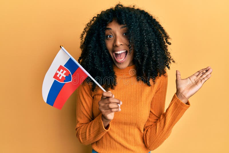 Afroameričanka s afro vlasmi drží vlajku slovenska oslavuje úspech so šťastným úsmevom a víťazným výrazom