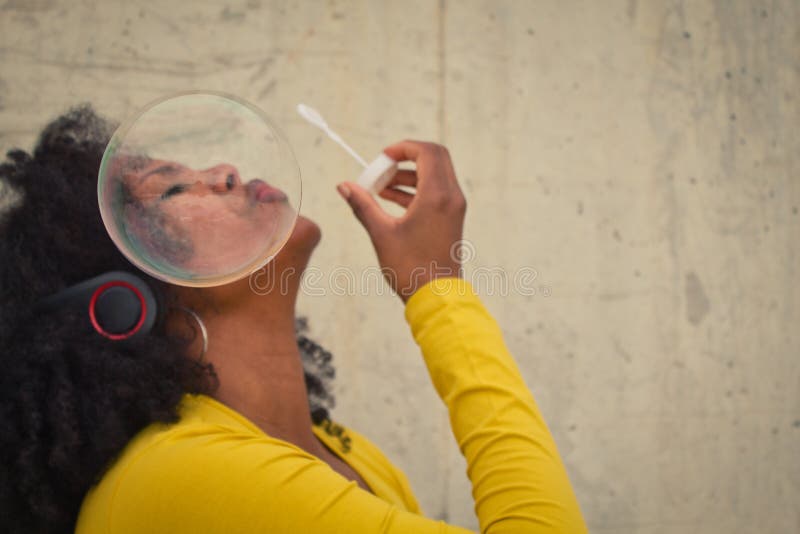 African american woman with afro hair and yellow t-shirt blowing soap bubbles