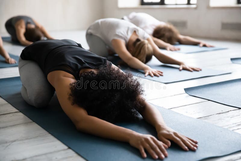 African American woman doing Balasana exercise at group yoga lesson