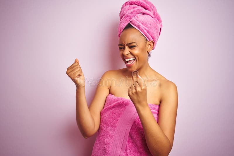 African american woman wearing shower towel after bath over pink  background very happy and excited doing winner gesture