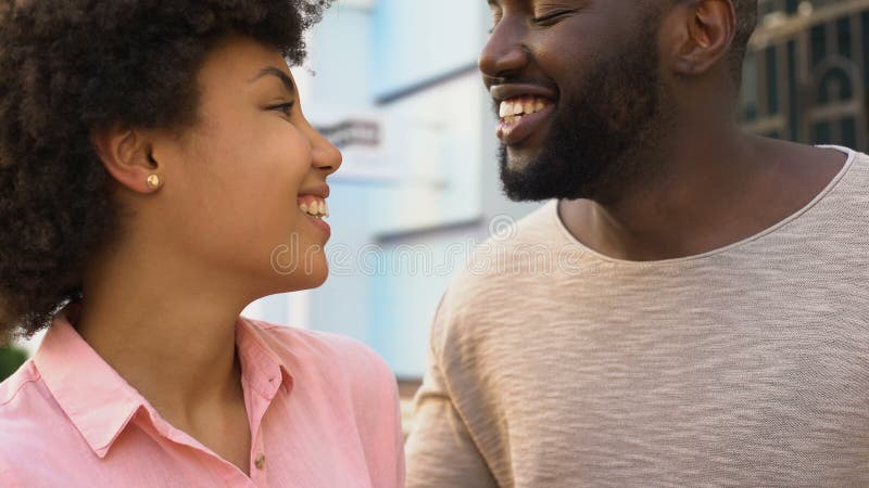 African boyfriend whispering words of love to girlfriend, happy smiling couple