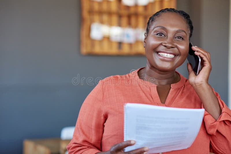 African businesswoman using a cellphone and reading documents at work