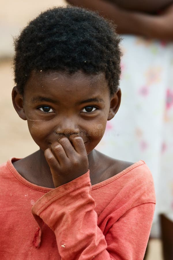 Un giovane bambino Africano in camicia rossa sorride alla macchina fotografica, rappresenta la povertà e problemi sociali in Africa.