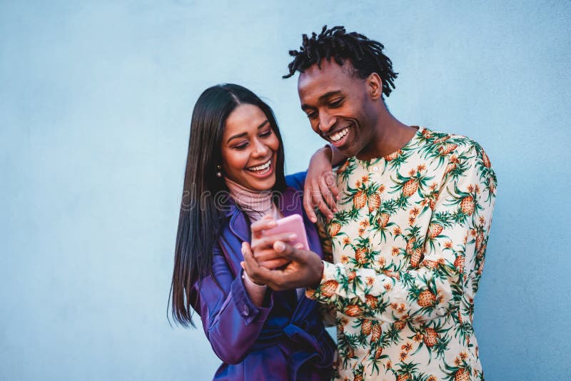 African couple watching videos on smartphone - Young people having fun shopping online with new trend technology - Youth, tech addiction, love and fashion concept - Soft focus on men face