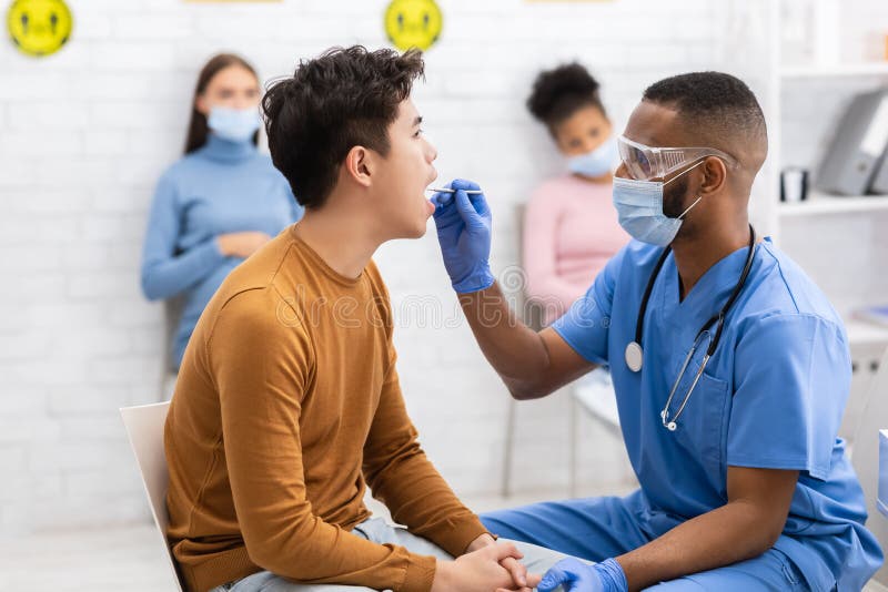 African Doctor Testing Asian Patient For Coronavirus Sitting In Clinic