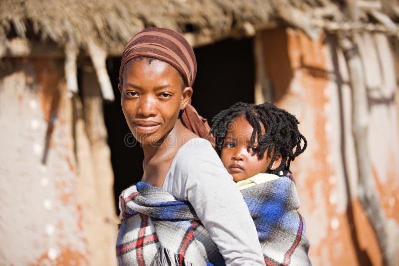 Afrikanische Mutter tragen Kind in einer traditionellen Art und Weise vor die Hütte.