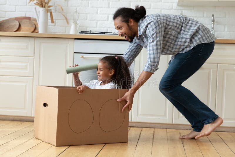 African father rides his little daughter in carton box stock photos