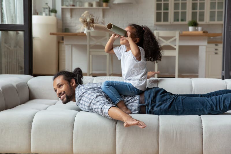 African girl sit on daddy back looks into paper tubes stock photos
