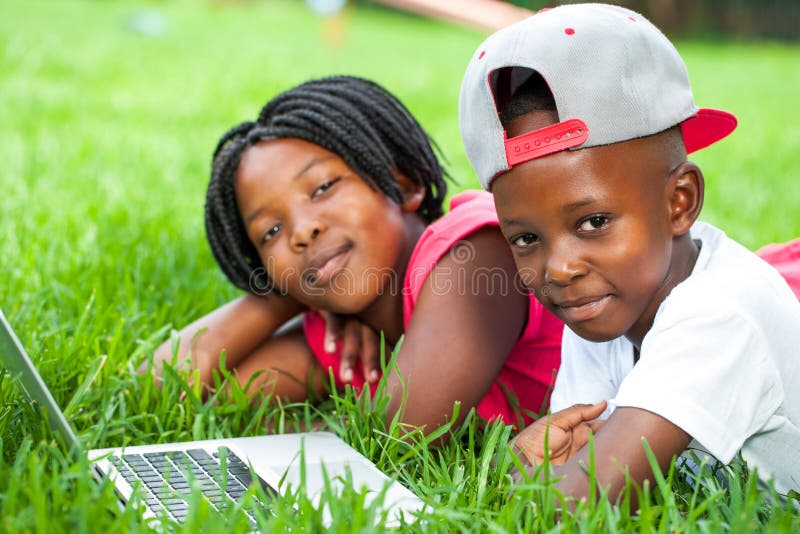 African kids laying on grass with laptop.