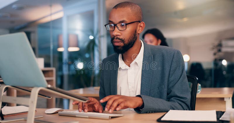 African man, computer and typing at office, night and editing proposal with overtime at media company. Person, editor and writer by pc with glasses for deadline, project or time management at agency. Computer editing stock images, royalty-free photos and pictures