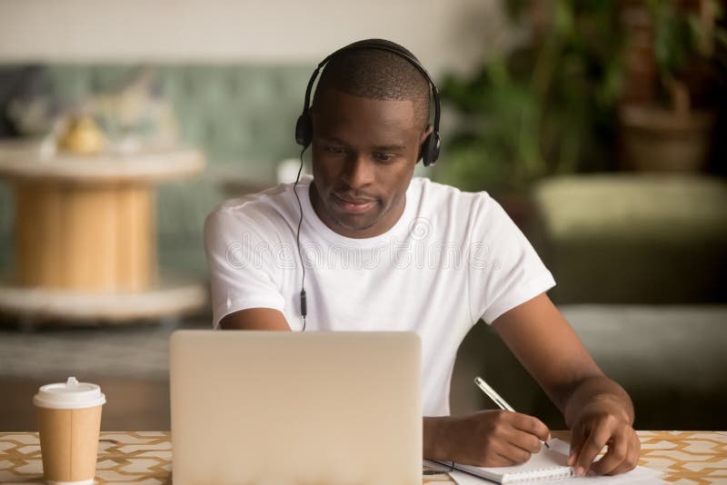 African man wearing headphones watching webinar making notes study online