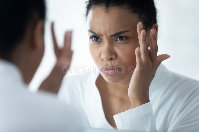 Frown African woman wear white bathrobe looking in mirror see first mimic wrinkles feels stressed, face skin lose elasticity changes after 30s, aging process, need cosmetology facial treatment concept. Problem wrinkle stock images, royalty-free photos and pictures