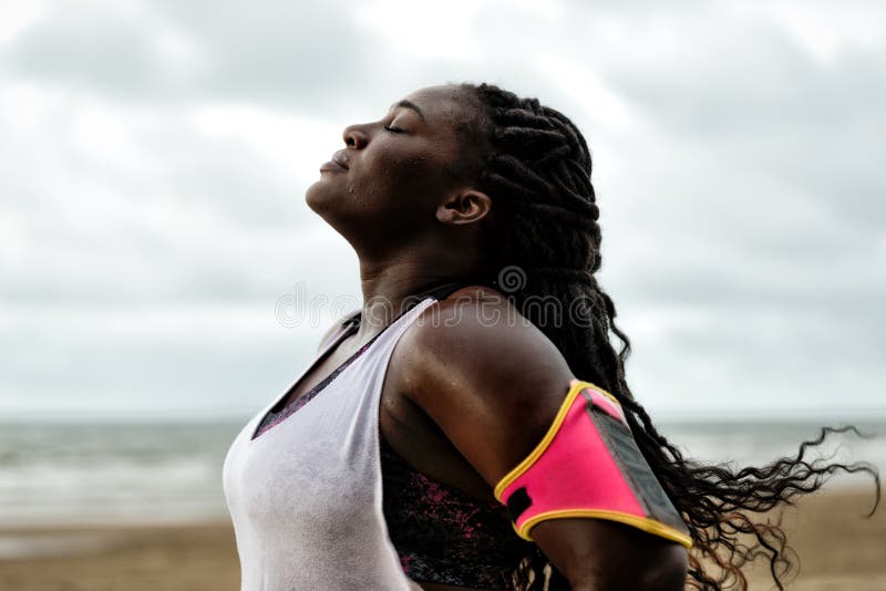 African woman standing under the rain,eyes closed, after workout on beach