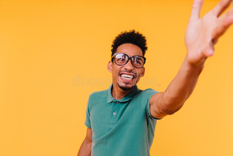 Africano sicuro di sé che cerca e alza la mano. ritratto interno di un modello maschile riccio in grande vetro fotografia stock libera da diritti