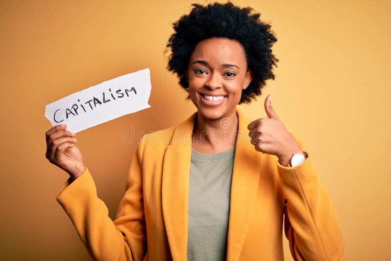 African American afro businesswoman with curly hair holding paper with capitalism message happy with big smile doing ok sign, thumb up with fingers, excellent sign. African American afro businesswoman with curly hair holding paper with capitalism message happy with big smile doing ok sign, thumb up with fingers, excellent sign