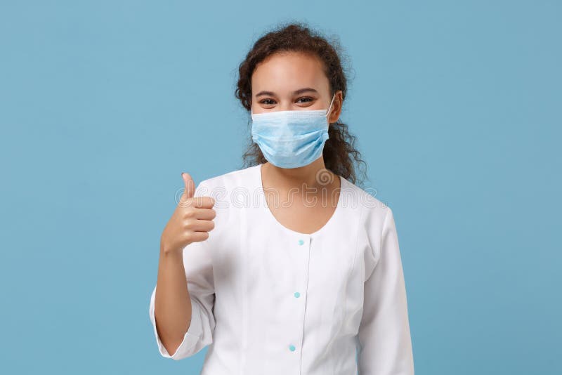 African american doctor woman isolated on blue background. Female doctor in white medical gown, sterile face mask showing thumb up. Healthcare personnel health medicine concept. Mock up copy space. African american doctor woman isolated on blue background. Female doctor in white medical gown, sterile face mask showing thumb up. Healthcare personnel health medicine concept. Mock up copy space