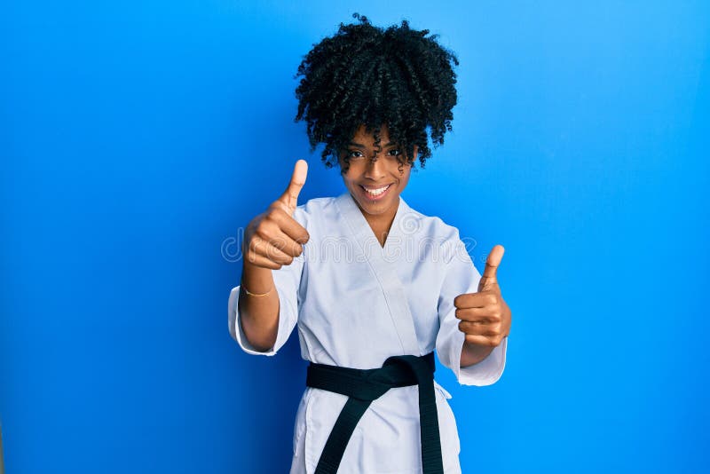 African american woman with afro hair wearing karate kimono and black belt approving doing positive gesture with hand, thumbs up smiling and happy for success. winner gesture. African american woman with afro hair wearing karate kimono and black belt approving doing positive gesture with hand, thumbs up smiling and happy for success. winner gesture
