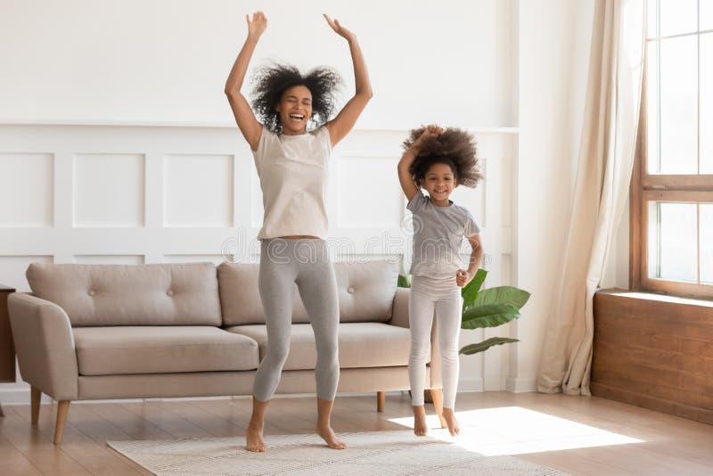 Afrikaans mamma met jong geitjemeisje springen die in woonkamer dansen stock foto's Afrikaans mamma met jong geitjemeisje springen die in woonkamer dansen stock foto's