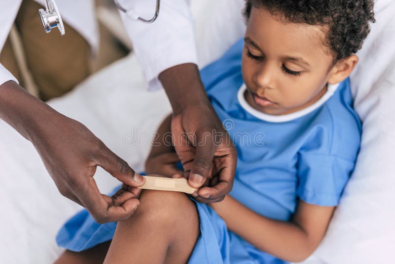 Cropped shot of african american doctor putting on adhesive plaster on childs knee. Cropped shot of african american doctor putting on adhesive plaster on childs knee