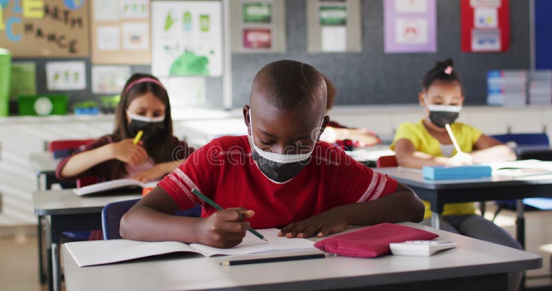 Afrikaanse amerikaanse jongen die een gezichtsmasker draagt terwijl hij in de klas studeert
