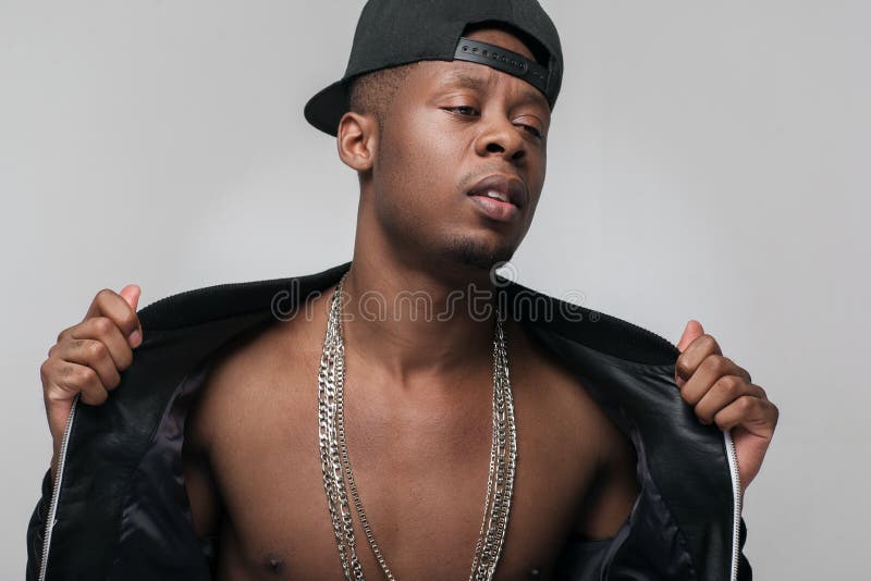 Young afroamerican rapper in hip-hop outfit on grey background. Problem of substance abuse, crime, social issues, drugs. Ghetto, challenge to society, cheeky, cool, rebellious. Young afroamerican rapper in hip-hop outfit on grey background. Problem of substance abuse, crime, social issues, drugs. Ghetto, challenge to society, cheeky, cool, rebellious.
