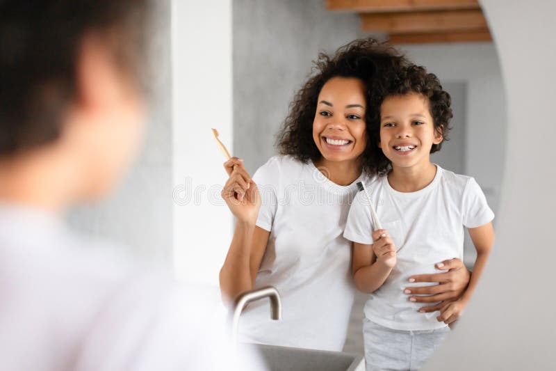 African American women and a child standing in front of a bathroom mirror, brushing their teeth with toothbrushes and toothpaste. African American women and a child standing in front of a bathroom mirror, brushing their teeth with toothbrushes and toothpaste