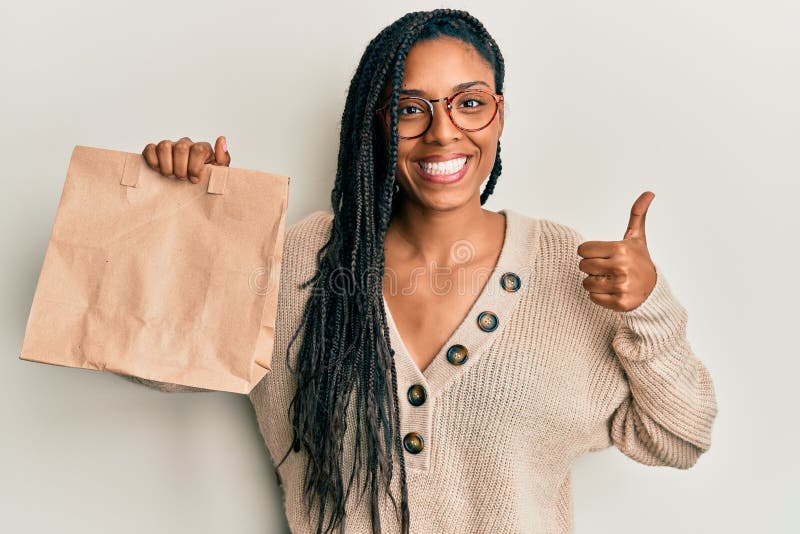 African american woman holding take away paper bag smiling happy and positive, thumb up doing excellent and approval sign. African american woman holding take away paper bag smiling happy and positive, thumb up doing excellent and approval sign