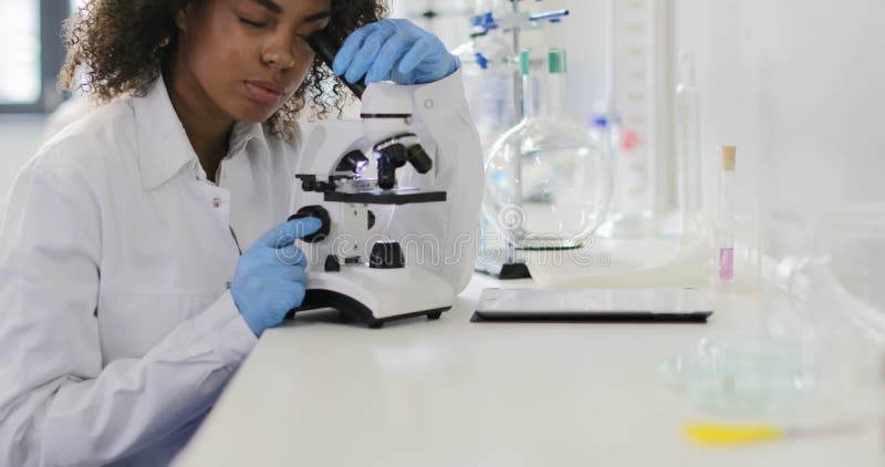 Afrikaanse Amerikaanse vrouwenwetenschapper die met microscoop in modern laboratorium werken die analyse maken