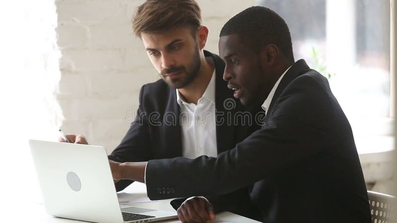 Afrikaanse Amerikaanse zakenman die PC-computerpresentatie tonen aan Kaukasische cliënt stock footage Afrikaanse Amerikaanse zakenman die PC-computerpresentatie tonen aan Kaukasische cliënt stock footage
