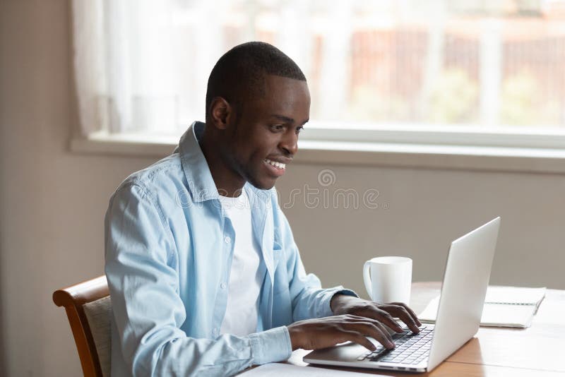 Afrikaanse millennial kerelzitting bij lijst het typen op laptop stock afbeelding Afrikaanse millennial kerelzitting bij lijst het typen op laptop stock afbeelding