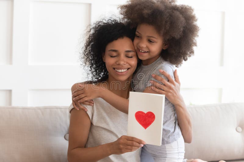 Afrikaanse mum die de groetkaart van de dochterholding op moedersdag koesteren stock fotografie Afrikaanse mum die de groetkaart van de dochterholding op moedersdag koesteren stock fotografie