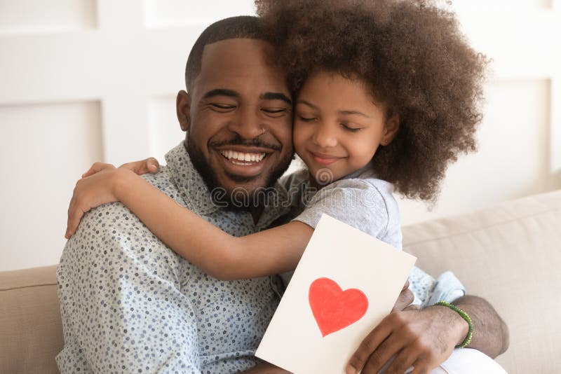 Happy affectionate african american dad embracing little child daughter holding greeting card with red heart bonding on fathers day concept, smiling cute kid girl hug daddy congratulate make surprise. Happy affectionate african american dad embracing little child daughter holding greeting card with red heart bonding on fathers day concept, smiling cute kid girl hug daddy congratulate make surprise