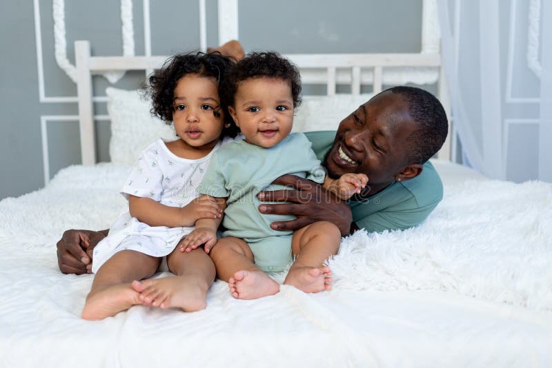 Afrikanamerikanischer papa spielt mit kindern babys zu hause auf dem bett im schlafzimmer und kuscheln väter liebe