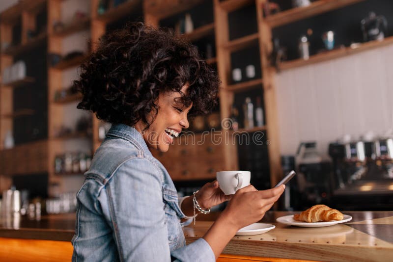 Afrikanerincafé unter Verwendung des Handys und des Lächelns lizenzfreie stockfotografie Afrikanerincafé unter Verwendung des Handys und des Lächelns lizenzfreie stockfotografie