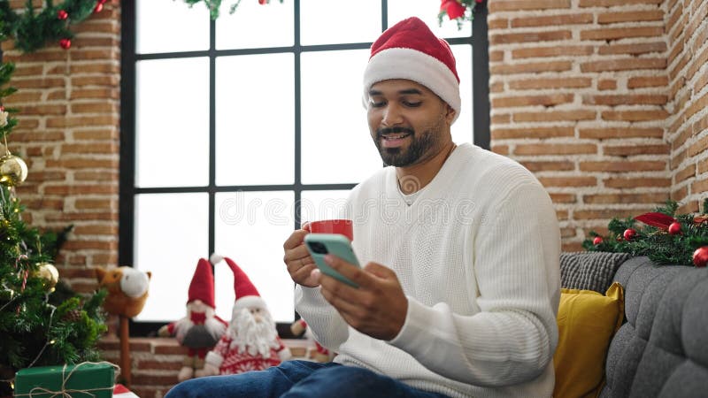 Afrikanischer Amerikaner, der mit Smartphone Kaffee trinkt und Weihnachten zu Hause feiert stockfoto