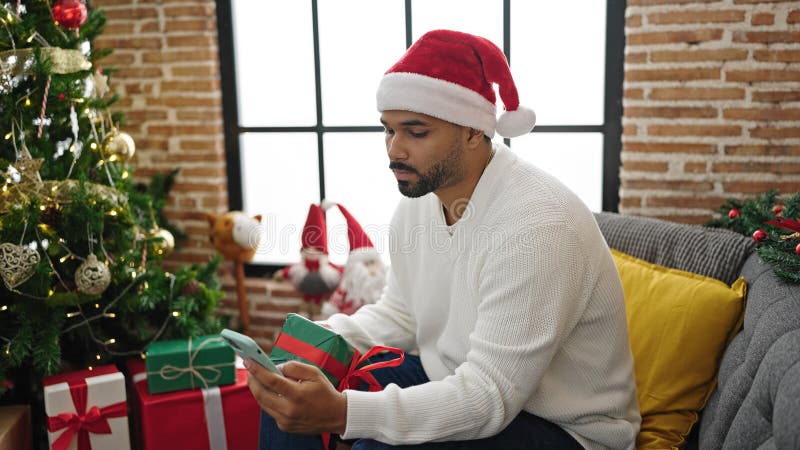 Afrikanischer Amerikaner mit Smartphone mit Weihnachtsgeschenk zu Hause lizenzfreie stockbilder
