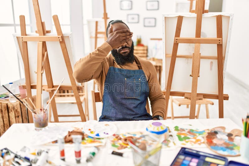 African american artist man at art studio smiling and laughing with hand on face covering eyes for surprise. blind concept. African american artist man at art studio smiling and laughing with hand on face covering eyes for surprise. blind concept