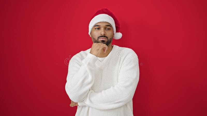 Afrikanischer amerikanischer Mann mit ernster Ausdruckskraft, der Weihnachtsmützen über isolierten roten Hintergrund trägt stockfotos