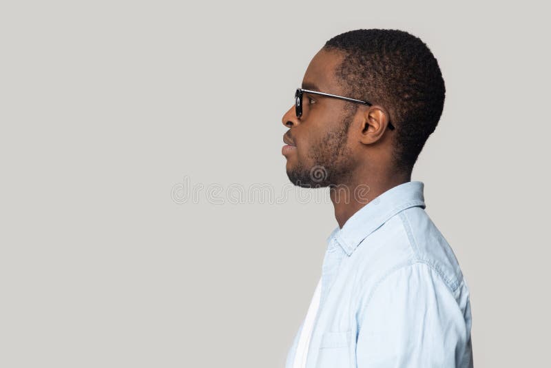 African dark-skinned man in casual blue shirt black framed glasses isolated on gray wall side profile view face, copy space for advertisement text, services promotion, motivated wise thoughts concept. African dark-skinned man in casual blue shirt black framed glasses isolated on gray wall side profile view face, copy space for advertisement text, services promotion, motivated wise thoughts concept