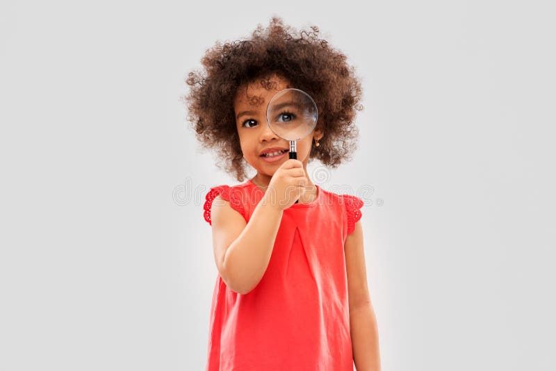 Investigation, discovery and vision concept - happy little african american girl looking through magnifying glass over grey background. Investigation, discovery and vision concept - happy little african american girl looking through magnifying glass over grey background