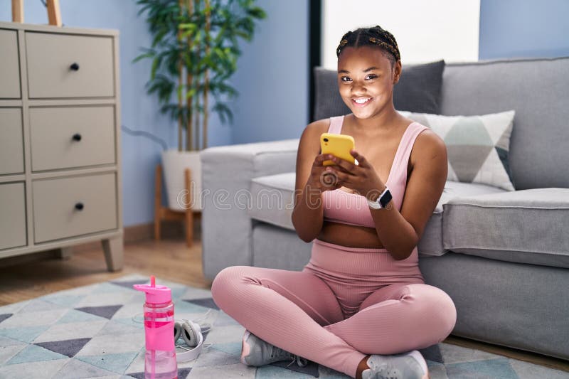 Afrikansk amerikan kvinna som använder smartphone som sitter på golvet hemma royaltyfria bilder
