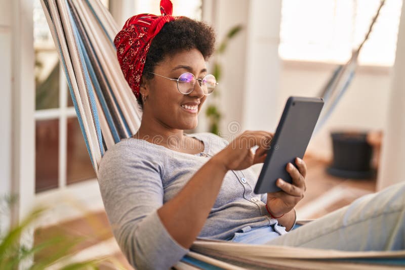Afrikansk amerikan kvinna som använder touchpad som ligger på hammock på hemterace